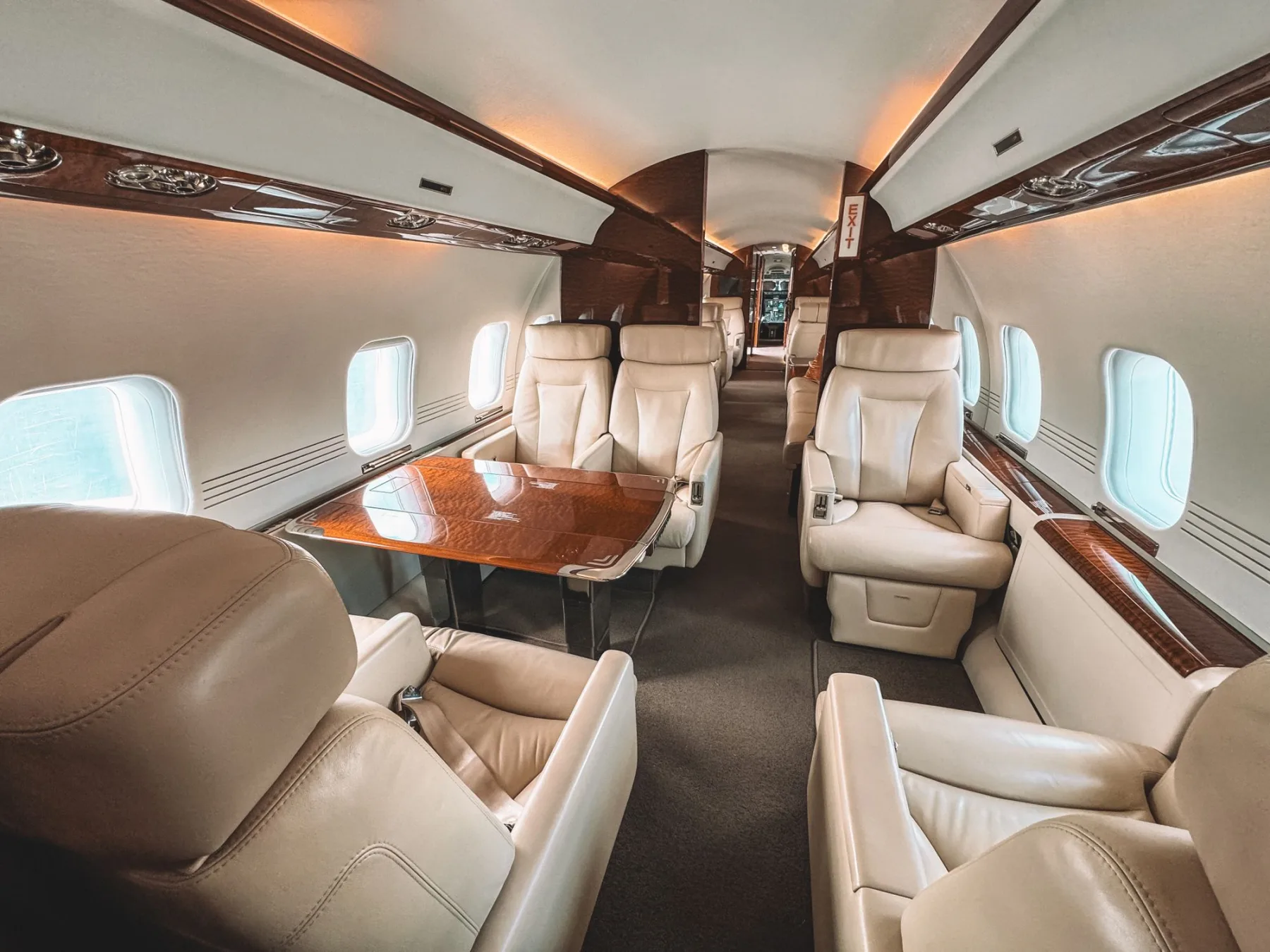 The cabin of a business jet, cream leather seating around a burl wood table